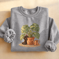 Black Cat Monstera Plant Sweatshirt, black cat peeking from a monstera plant, for cat lovers and plant moms